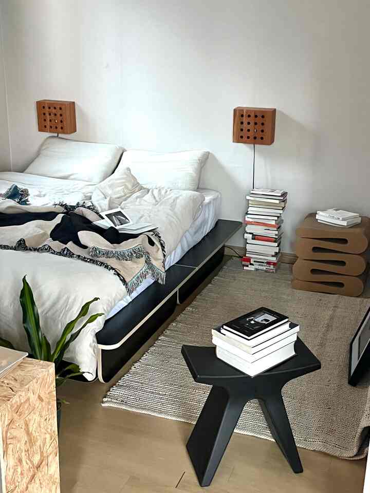 A modern natural bedroom featuring white walls, brown wooden floors, black bed frame and beige rug
