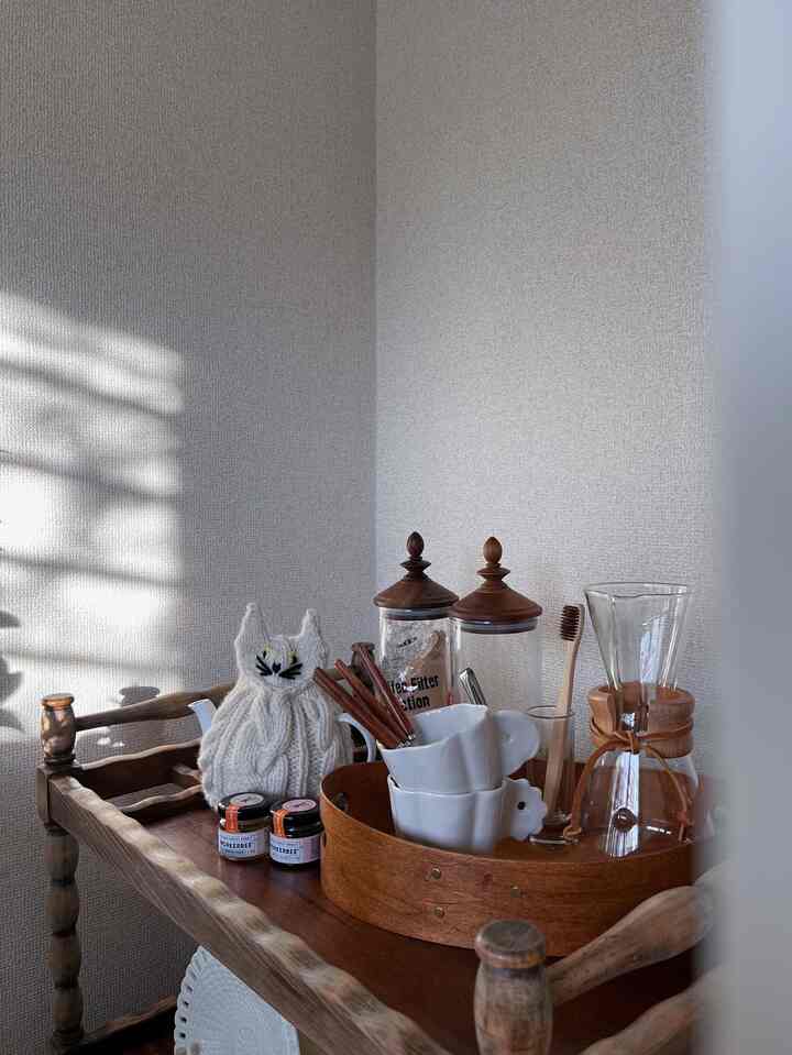 Natural wood tone kitchen cart with coffee accessories and tray arranged on a white-wall vintage-style kitchen space