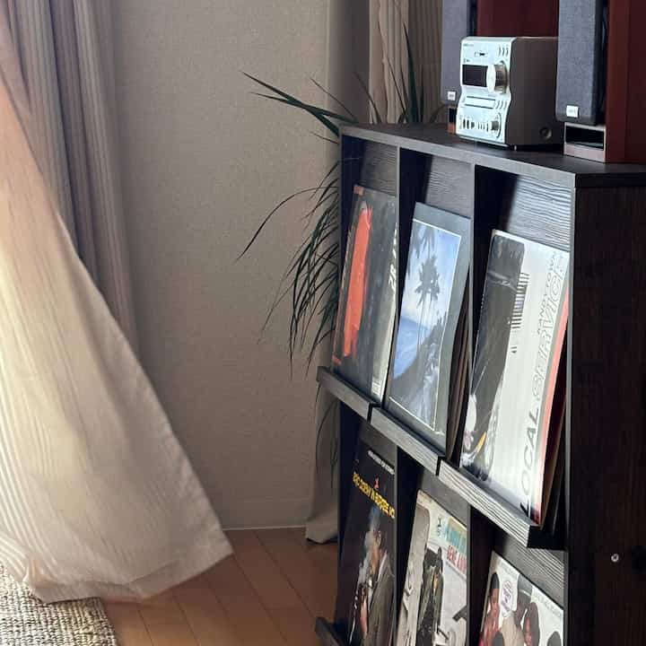 ナチュラルな木目調のリビング、LP収納ラックにレコードとカーテン、植物が配置された落ち着いた雰囲気のインテリア