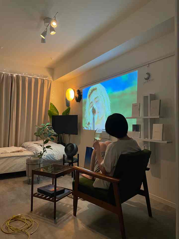 Warm natural-toned bedroom and living space featuring a home cinema projection on wall and wooden frame armchair creating cozy interior