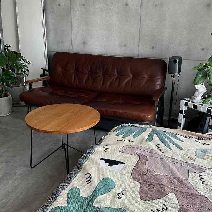 Natural cafe-style living room with gray concrete wall, wood tone round table, and dark brown leather sofa
