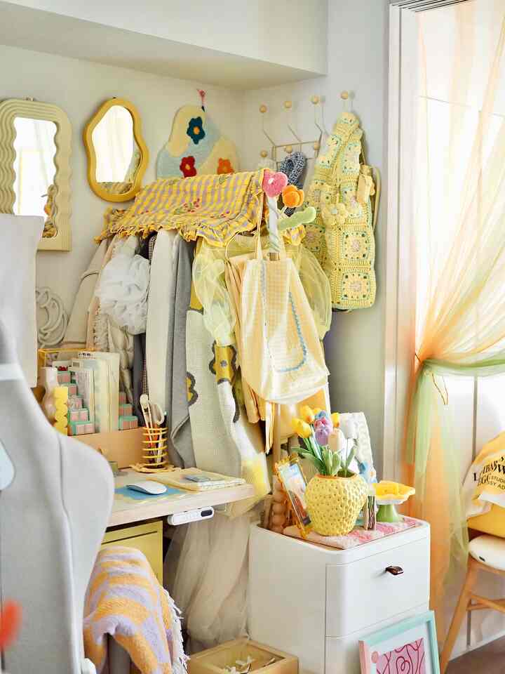 黄色と白のトーンの小さなホームオフィス空間、デスク横に縦型のコートラックとカーテンが配置された雰囲気のあるインテリア