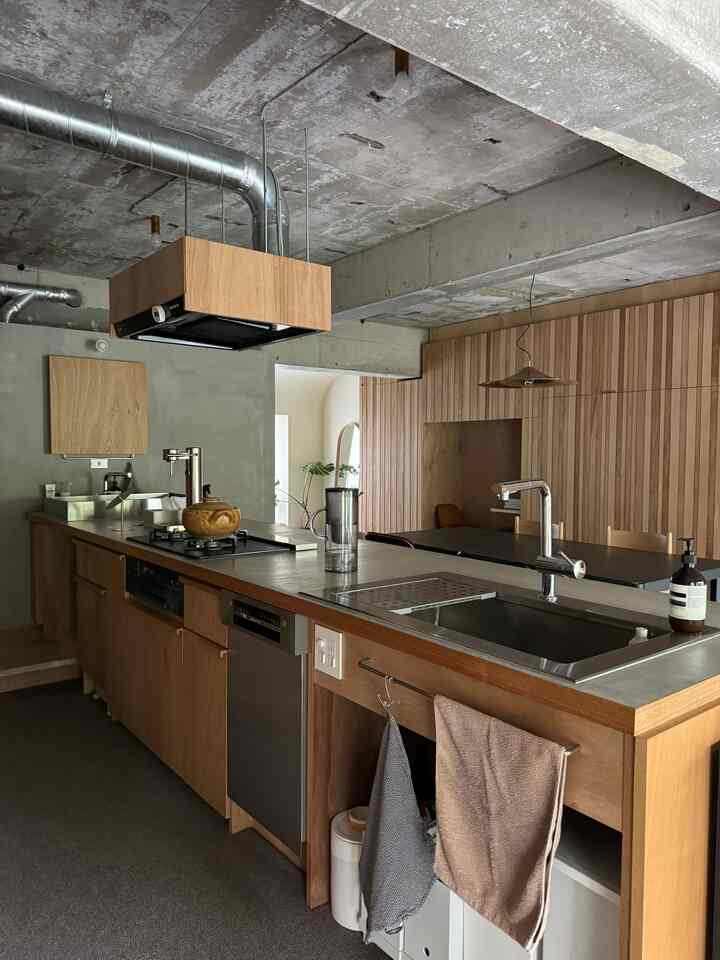 Modern kitchen with natural wood tones and exposed concrete ceiling, featuring carpeted floor and pendant lighting
