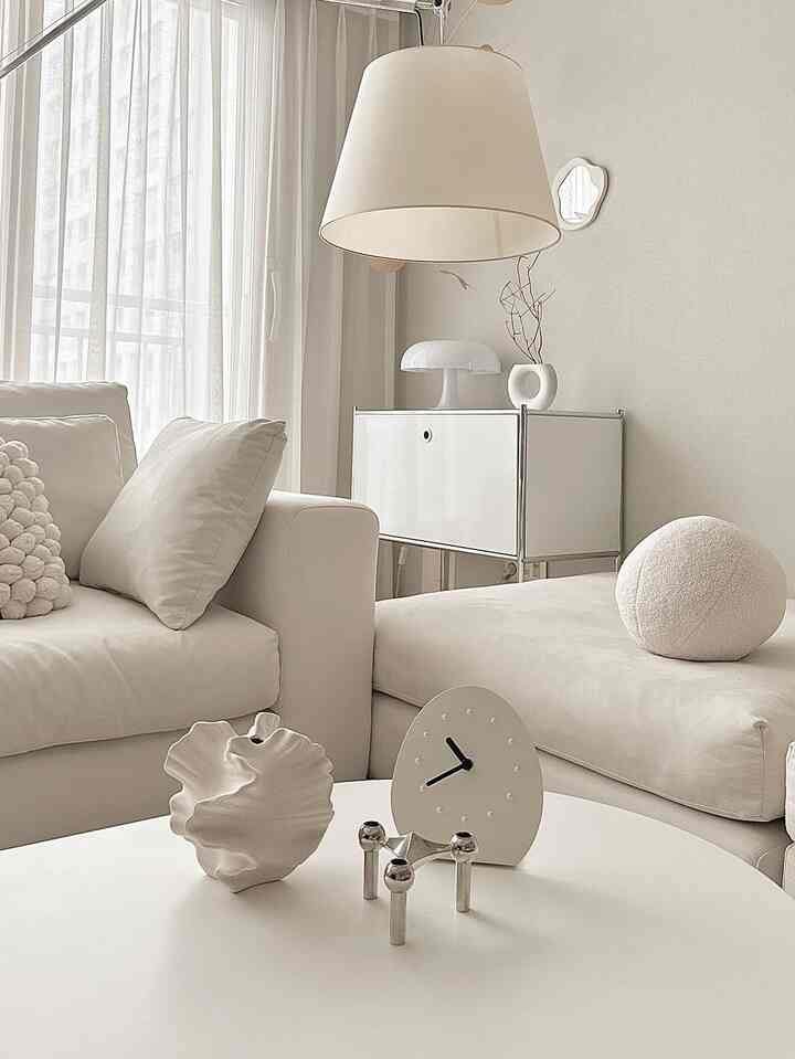 柔らかな白色調のリビングルーム、ゆったりとしたソファとシンプルなテーブル、モダンな照明が調和した印象的な空間