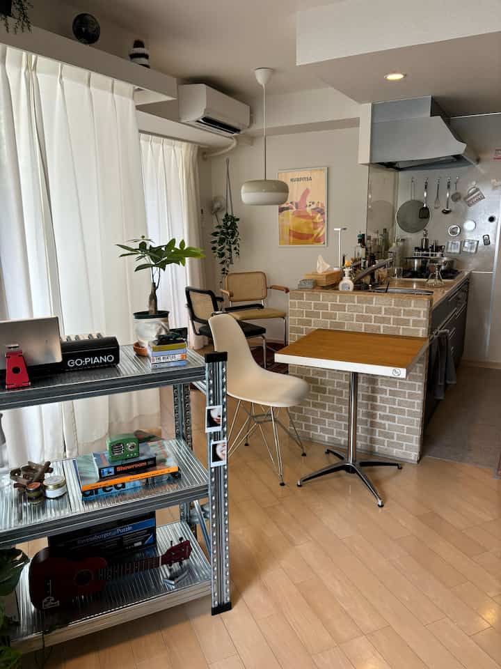 ナチュラルな色調の小さなキッチンとダイニングスペース、白いシェルチェアとラタンチェアが配置された雰囲気のあるモダンなカフェ風インテリア