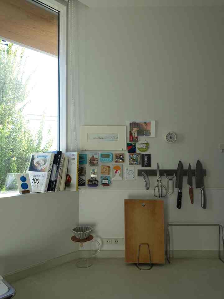 白を基調としたキッチンの壁、マグネット式の包丁スタンドとまな板、本が配置された清潔感と自然光があるインテリア