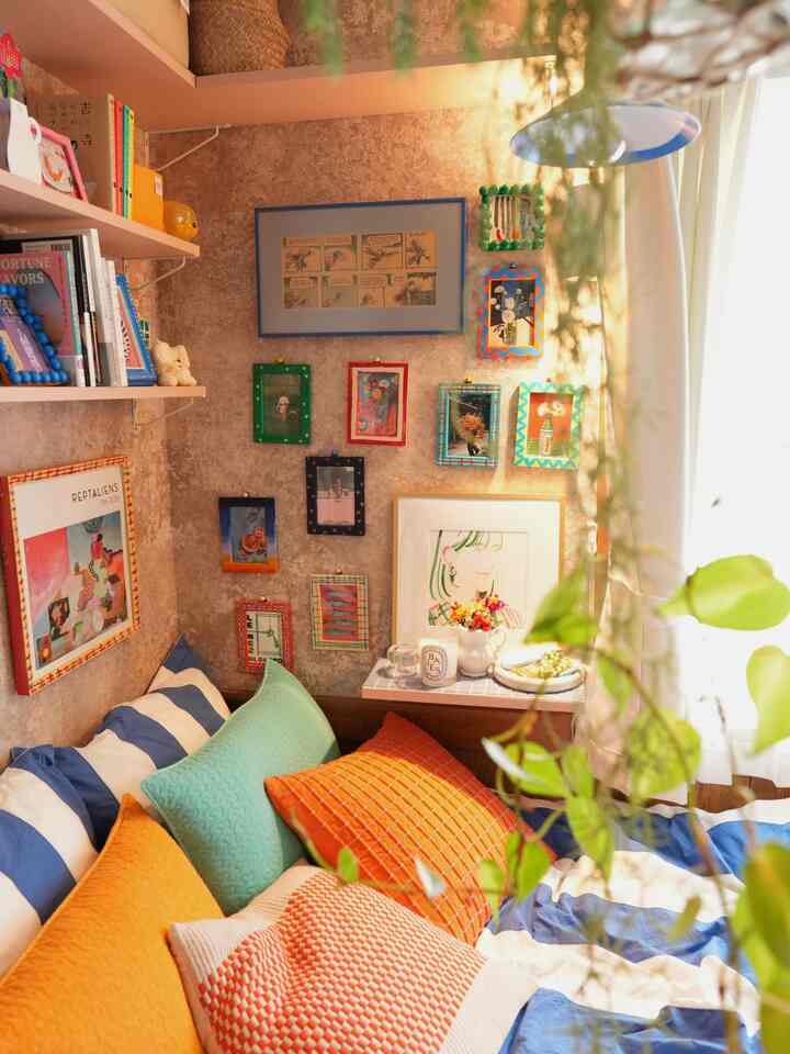 温かみのあるオレンジと青のクッションが並ぶ、白と青のストライプベッドがあるナチュラルな寝室