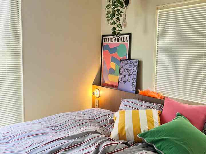 Bright white-toned bedroom featuring striped bedding, colorful cushions, and posters styled in Mid-Century Modern theme