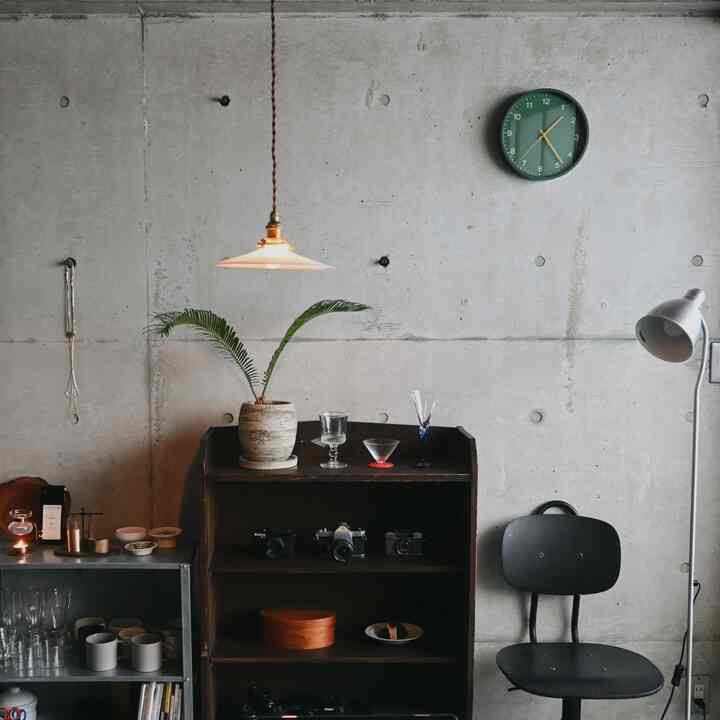 Gray concrete wall with wooden shelf, black stool, and silver floor lamp in an industrial-style living room