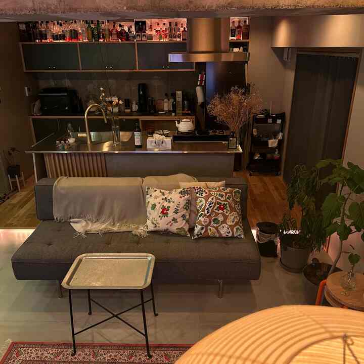 Natural wood tone modern living room with open kitchen and home cafe atmosphere featuring sofa, plants, and bar elements