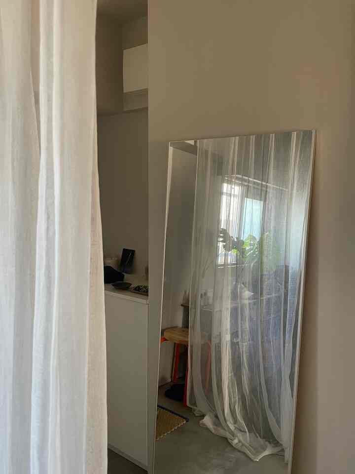 白とナチュラルな色調の玄関、シアーカーテンとモダンなスツールが配置された落ち着いた雰囲気のインテリア