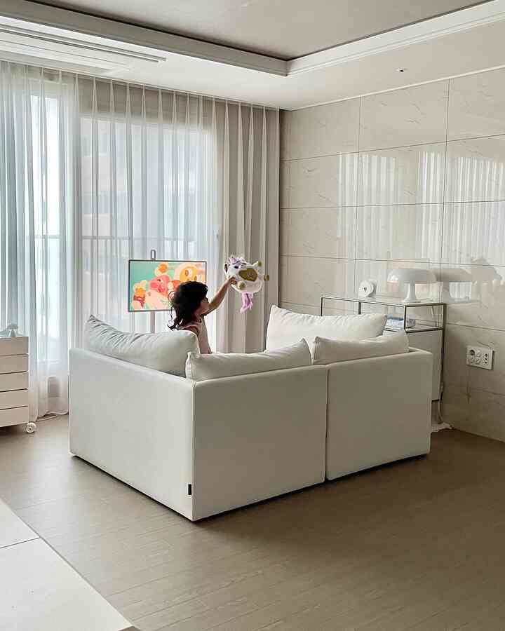 白を基調としたリビング、中央に大きなモジュールソファと遊ぶ赤ちゃんが見える、明るく広々とした印象的な空間