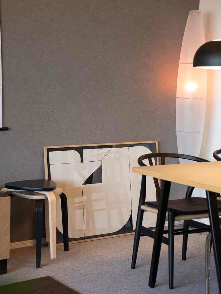 Natural modern dining room with wood tones and black accents, featuring a large modern poster leaning on the floor and a white floor lamp providing warm light