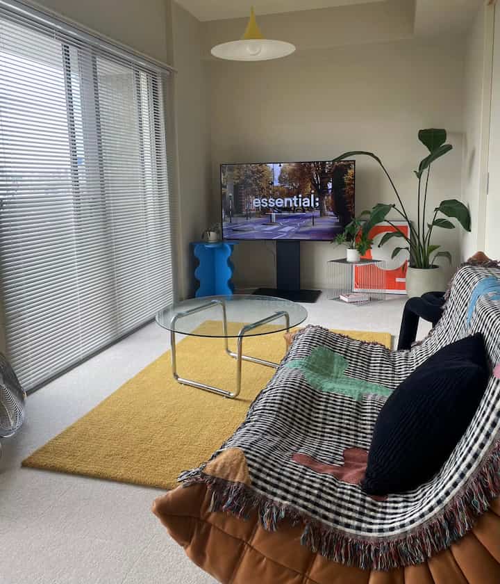 暖かいイエローとブラックのアクセントがあるリビング、茶色のソファにスローとクッションが置かれ、ガラステーブルと植物が配置された居心地の良い空間