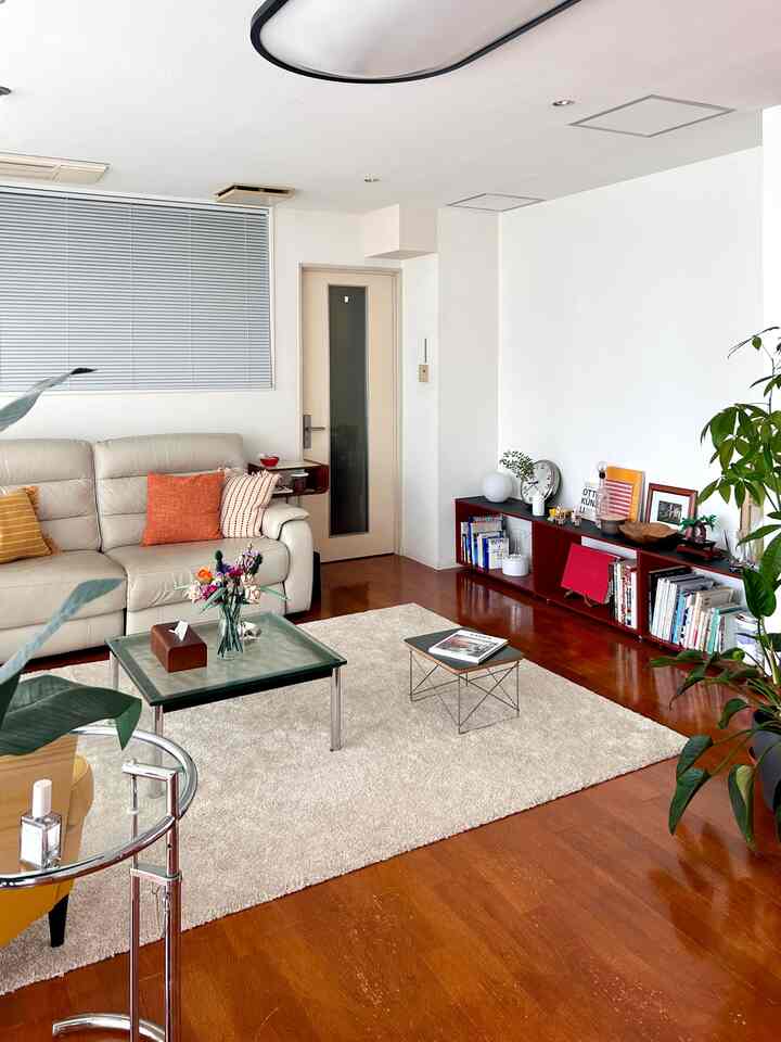 白とブラウンの木目調が調和するミッドセンチュリーモダンのリビング、ベージュのレザーソファとワイヤーベースのテーブル、ラグが配置された雰囲気のある空間