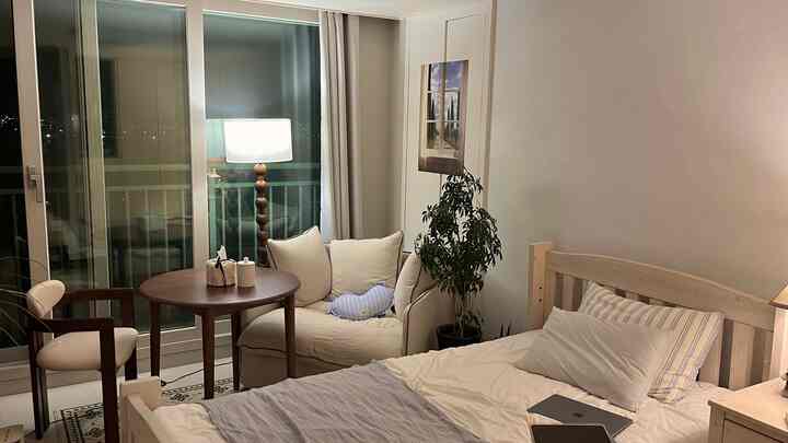 白と茶色のトーンでまとめられた寝室、木製家具とファブリックソファが配置されたシンプルでナチュラルモダンなインテリア