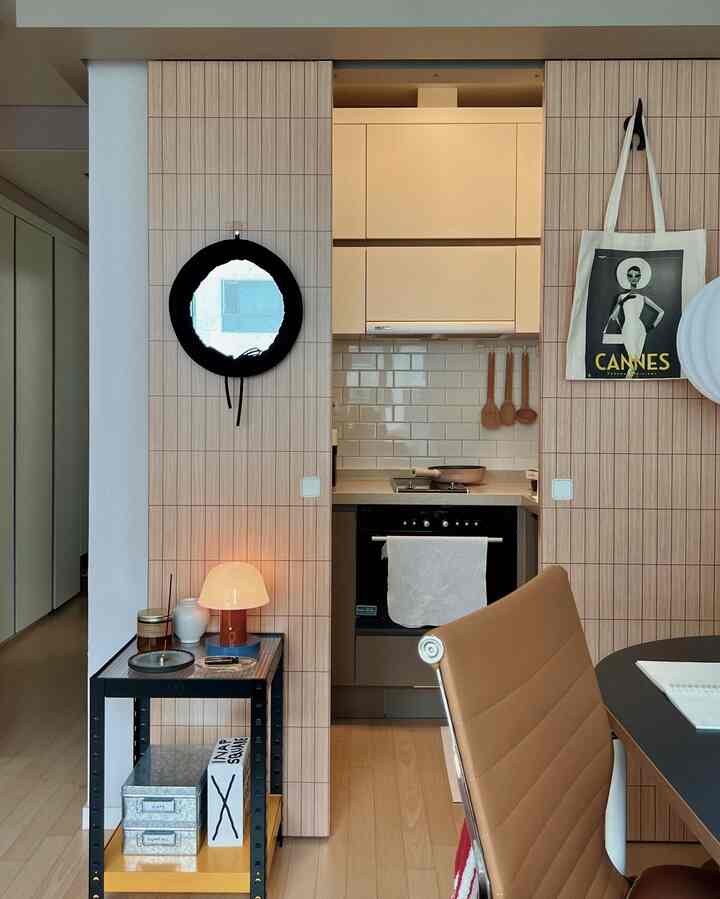 ウッドトーンでモダンな一人暮らし向けのコンパクトなキッチンとホームオフィス空間、テーブルランプとオフィスチェアが配置されたインテリア