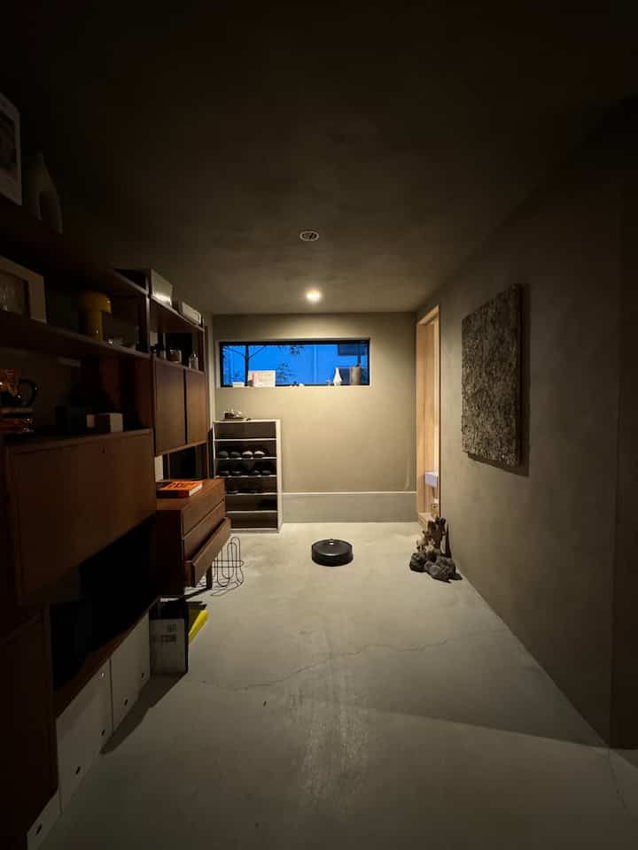 Beige-toned natural small entrance featuring large wooden bookshelf on left and a robot vacuum centered on minimalist floor