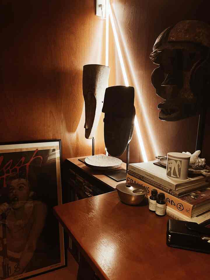 Warm brown-toned small study featuring neon lighting, African traditional masks, and a framed poster creating cozy ambiance