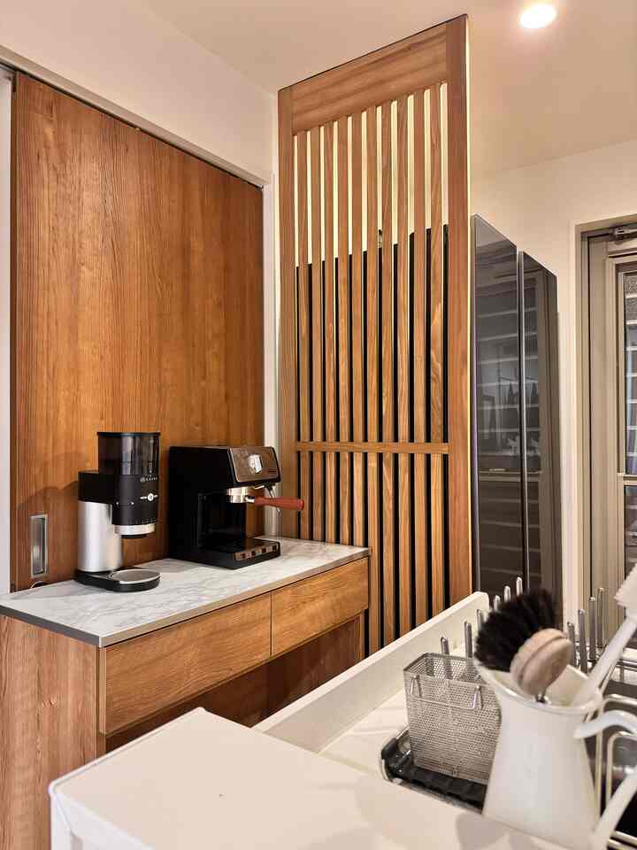 木目調と無機質素材が調和した温かみのあるキッチンのホームカフェ、洗練されたコーヒーマシンと木製スラットの壁装飾が印象的なインテリア