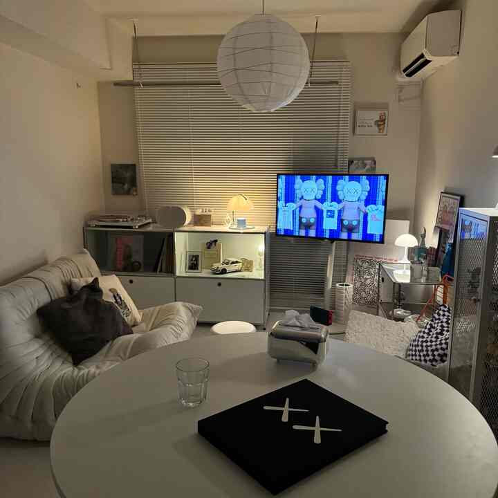 白を基調としたワンルームのリビング、モダンなソファとテーブルにKAWSのアートが配置された雰囲気のあるインテリア