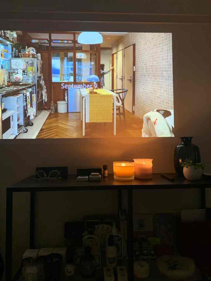 Warm wood-toned 1K living room for single household with candles on table and projector screen displayed on wall, cozy atmosphere