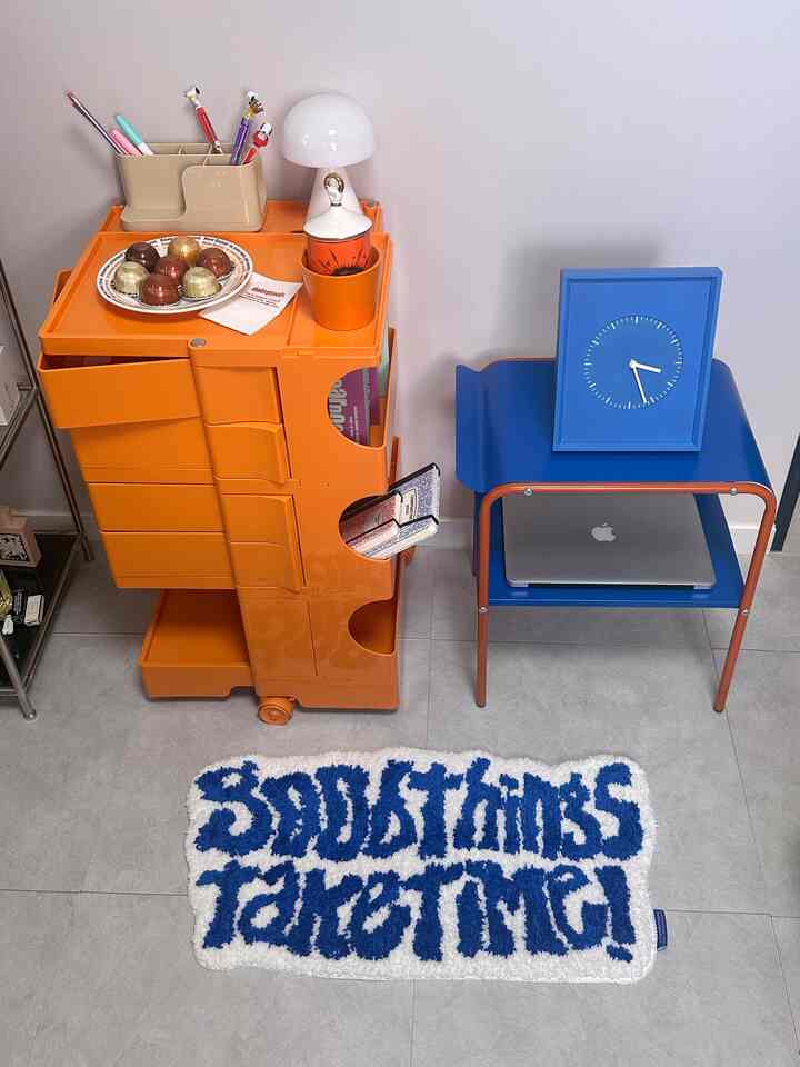 明るいオレンジのトローリーと青いサイドテーブルが配置された寝室の雰囲気のあるインテリア