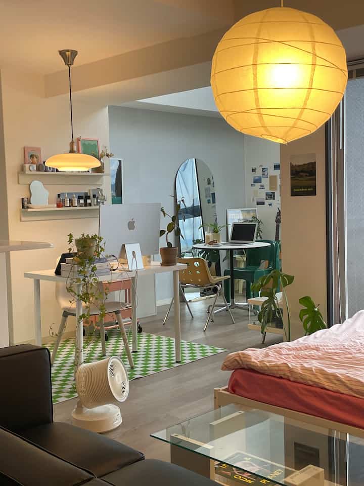 Modern studio apartment featuring white and wood tones with a desk, bed, and plants creating a clean and cozy atmosphere