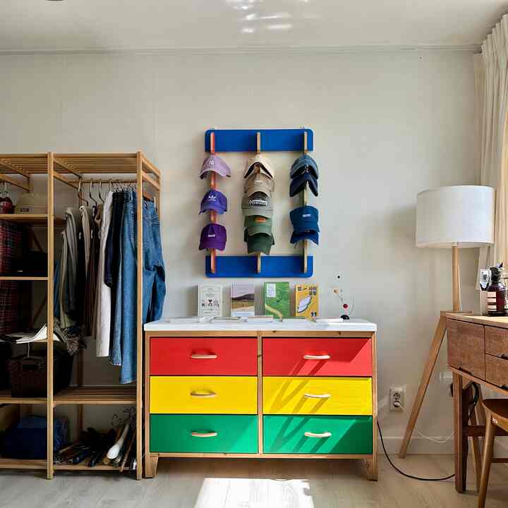 ナチュラルな色合いの寝室、赤・黄・緑の引き出しのチェスト、壁掛け帽子掛け、白いフロアランプが調和した温かみのあるインテリア