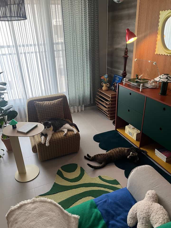 Natural tone living room with checkered armchair and sofa, two cats lounging, red floor lamp and sideboard creating cozy atmosphere