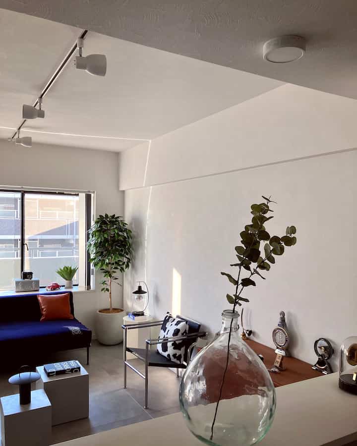 ホワイトの壁とネイビーのソファがあるナチュラルカラーのヴィンテージリビング、植物とモダンな家具を配置した空間