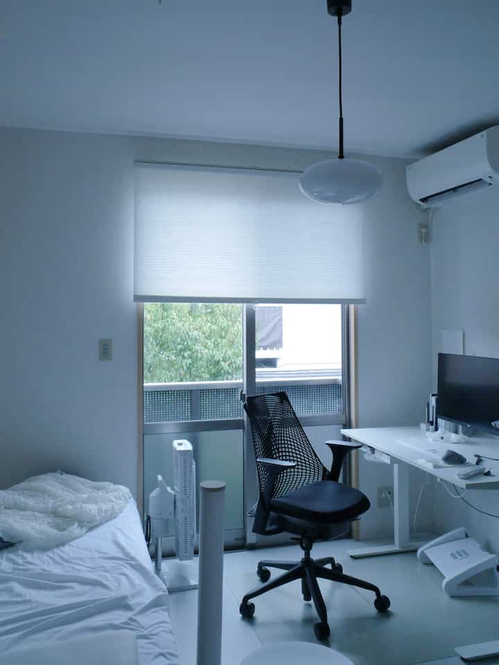 White-toned single household bedroom and home office featuring a clean desk setup, computer, and blinds controlling natural light