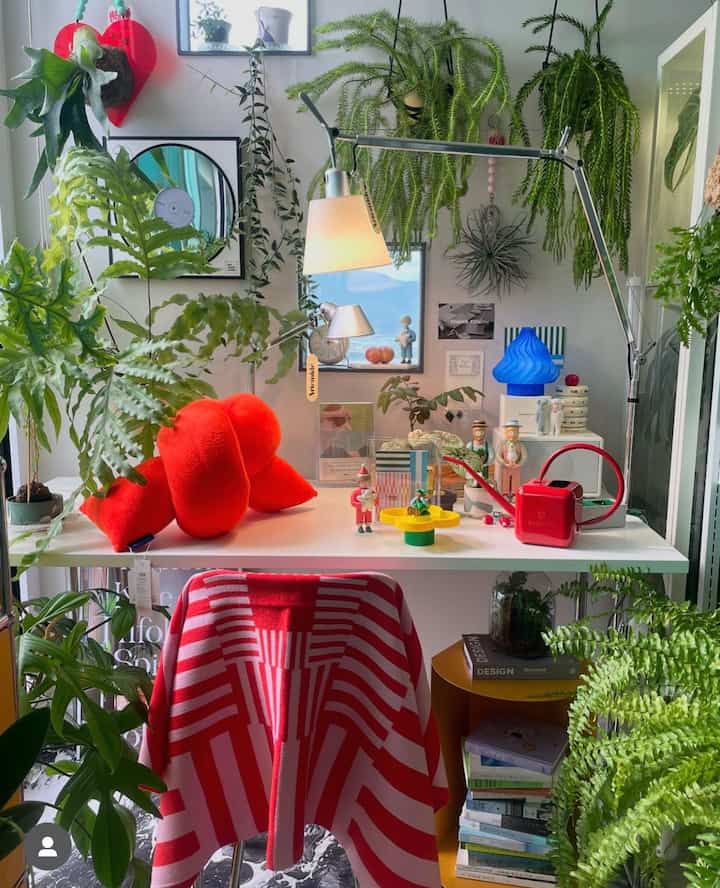 A cozy home office space with red and green tones, featuring a side table and various plants