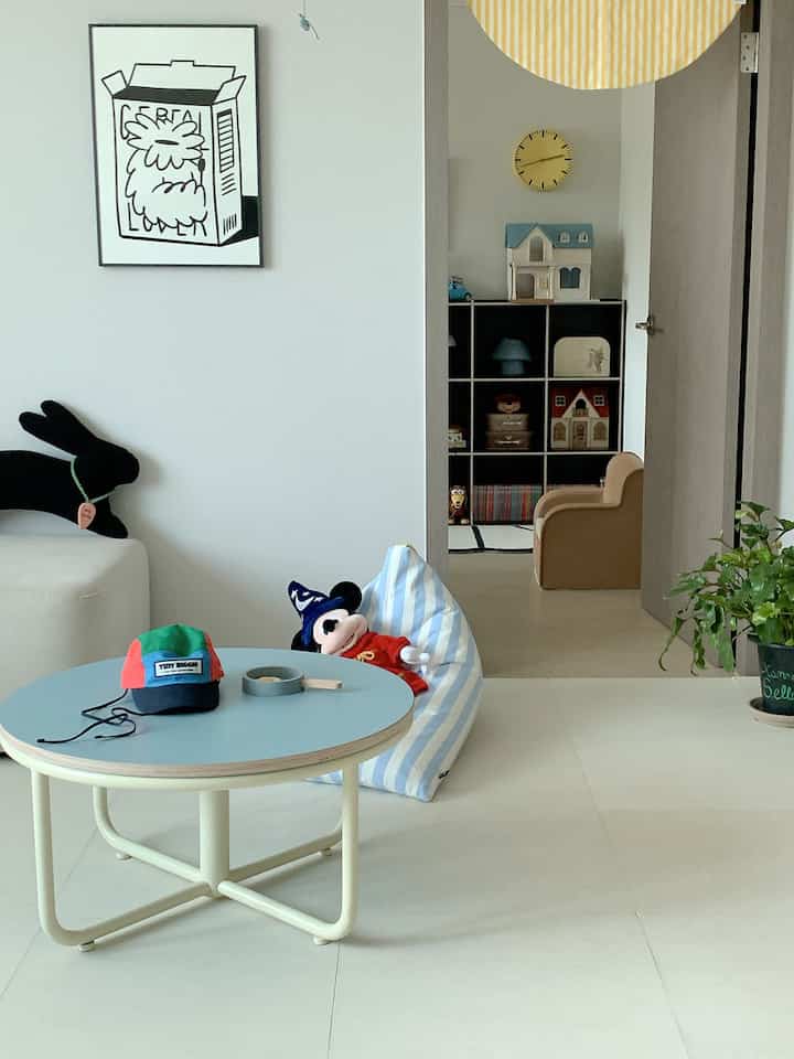 White walls and floors, sky blue round table and bean bag, clean Nordic style living room with a kids' play area visible