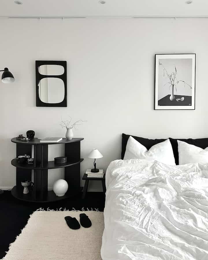 モノトーンの黒と白を基調にした寝室、整ったベッドとナイトテーブル、壁に黒い額縁のポスターが飾られた雰囲気のあるインテリア