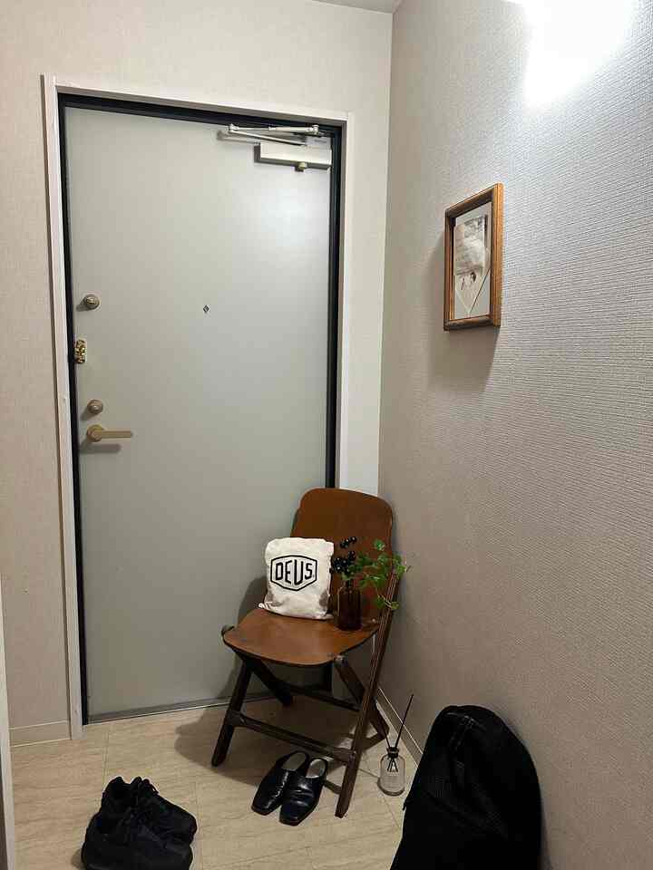 Beige tiled floor entrance featuring a wood-tone folding chair with plants and diffuser, creating a neat atmosphere