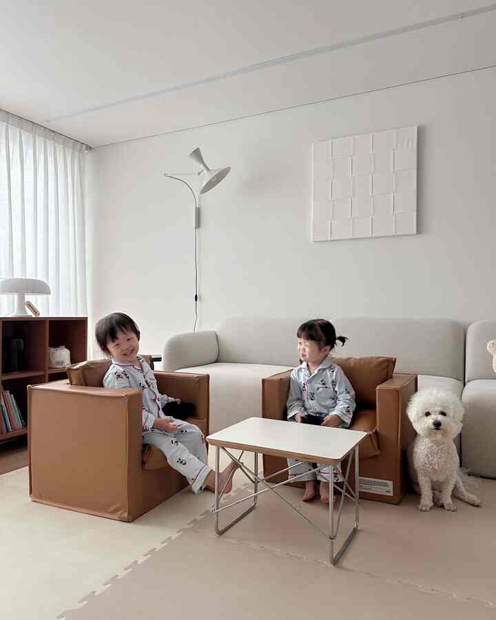 Natural-colored living room with white and brown tones, featuring two child armchairs, sofa, small table, and a dog creating a cozy atmosphere