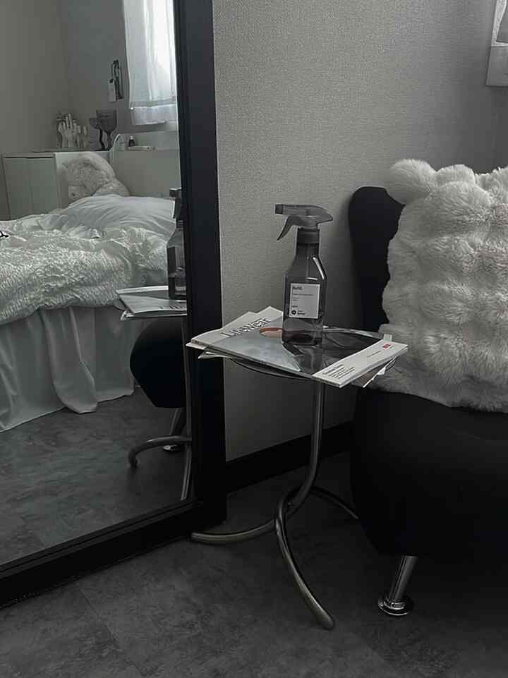 モノトーンでミニマルな寝室、全身鏡と黒いアームチェアが配置されたシンプルなインテリア