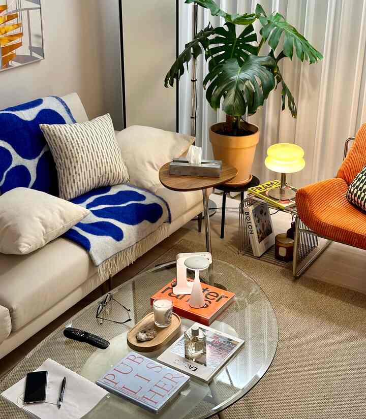 ナチュラルトーンのリビング、白いソファとオレンジのアームチェア、大きなモンステラが配置された暖かい雰囲気の空間