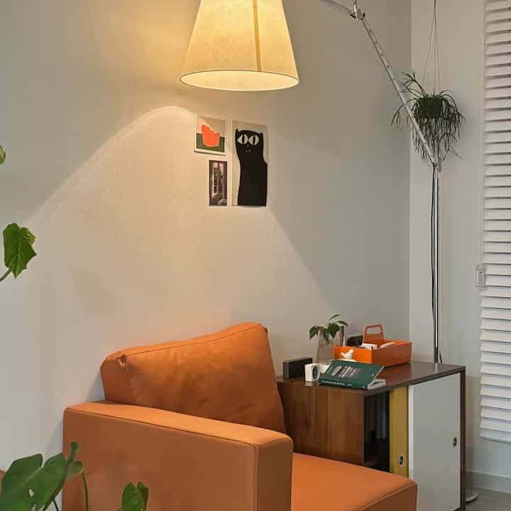 暖かいベージュの壁とオレンジ色のアームチェアがある居心地の良いリビング、サイドテーブルとフロアランプが配置された空間