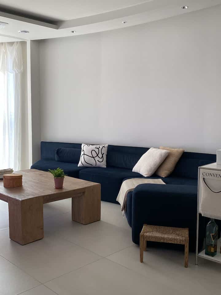 明るくシンプルなリビング、ネイビーのコーナーソファと木目調のコーヒーテーブルが配置されたインテリア