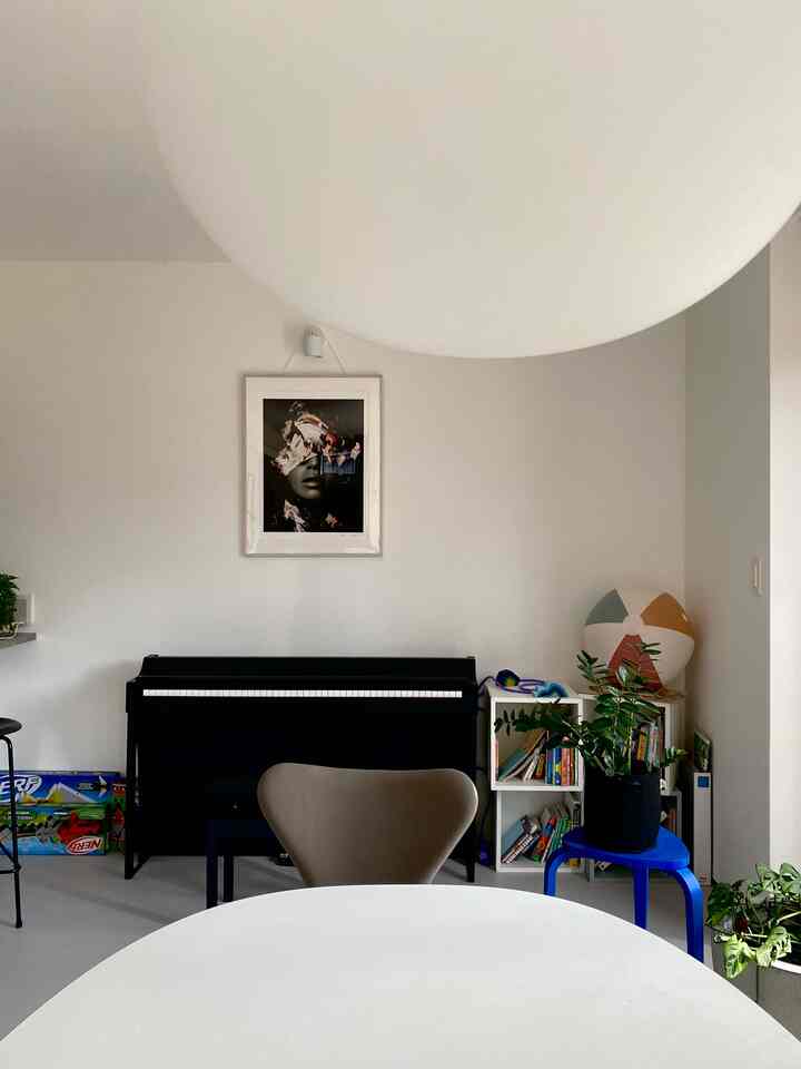 Natural tone dining room featuring a white table, black electronic piano, and kids' bookshelf with a calm atmosphere