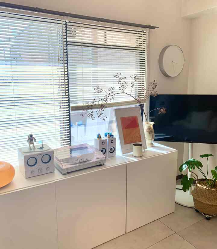 White-toned living room featuring a white storage cabinet with record player and picture frame, blinds creating a minimalist and modern interior