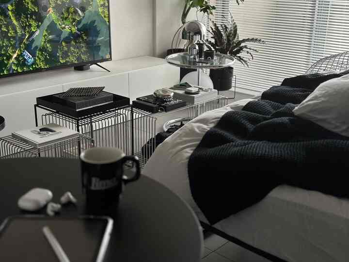 ブラックとホワイトトーンのモダンな寝室、ワイヤーフレームのサイドテーブルとクロームのテーブルランプが配置された雰囲気ある空間