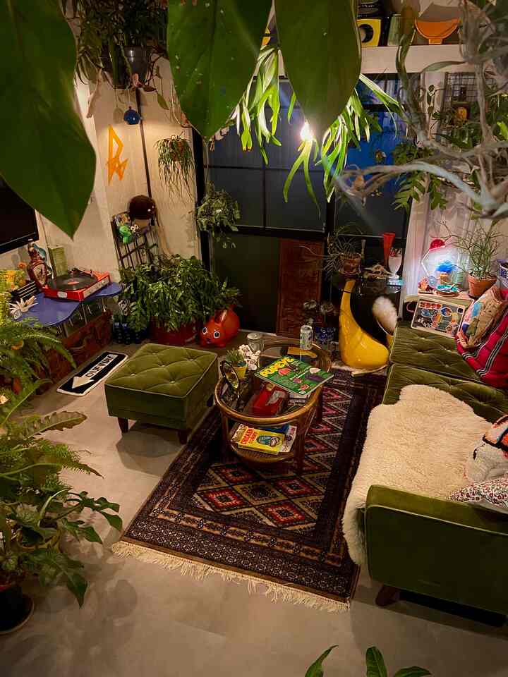 緑のソファとオットマン、多様な観葉植物が配置されたヴィンテージスタイルの落ち着いたリビング空間