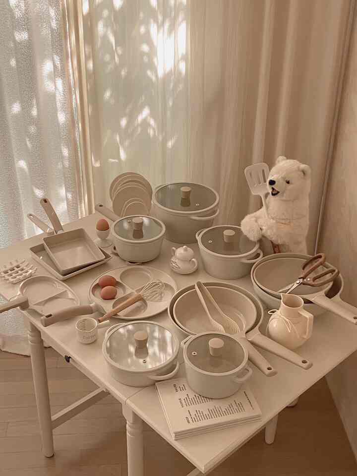 ベージュの色調のキッチン、テーブルにセラミック鍋や調理器具が配置された雰囲気のある空間