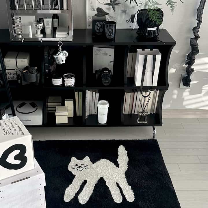 Black and white toned living room featuring a cat-patterned rug and organized storage rack in a minimal and modern interior