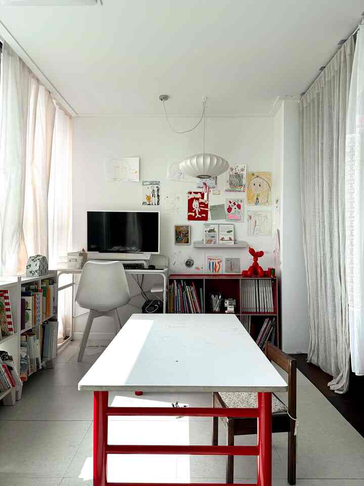 Bright white-toned living room featuring a kids' desk and red bookshelf with warm, inviting atmosphere