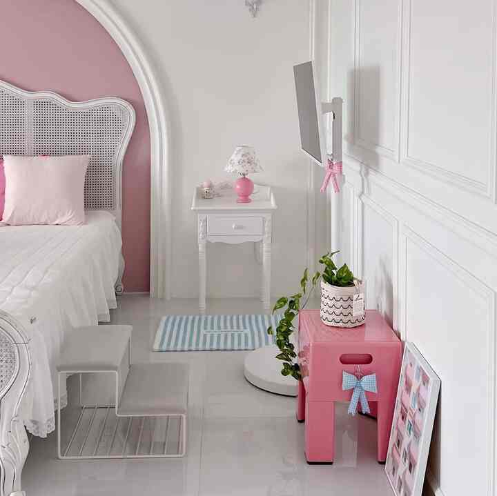 White and pink toned bedroom featuring a bed, wainscoting walls, dog steps, and charming decor elements