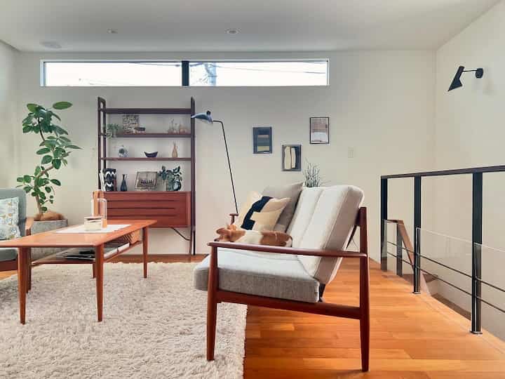 Natural-toned living room featuring wooden-framed sofas, a coffee table, a bookshelf by the window, and a dog resting comfortably